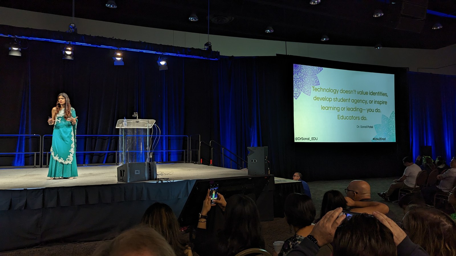 Dr. Sonal Patel on stage at a keynote in a teal Indian outfit, with a screen behind her reading an identity and equity quote